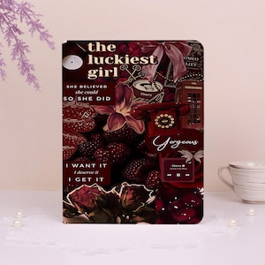 Könnte beinhalten: Ein rechteckiges Notizbuch mit einem dunkelroten Collage-Einband, der Erdbeeren, Rosen, ein Wählscheibentelefon, eine Telefonzelle und Text zeigt, darunter "the luckiest girl", "SHE BELIEVED she could SO SHE DID", "Gorgeous" und "I WANT IT I deserve it I GET IT."