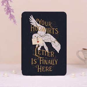 Op de afbeelding: Een zwarte e-reader hoes met een witte uil in vlucht die een crèmekleurige envelop met een rood waszegel draagt. De gouden tekst "YOUR HOGWARTS LETTER IS FINALLY HERE" staat op een donkere achtergrond met subtiele sterachtige spikkels.