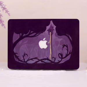 May include: A purple laptop skin featuring a dark forest silhouette with a tall tower and long flowing golden hair cascading down. The design incorporates the central white Apple logo, which is positioned to appear as part of the scene.