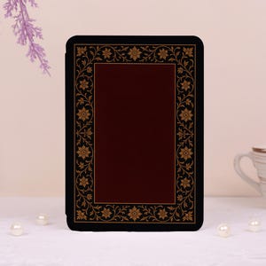 May include: A rectangular e-reader case featuring a deep burgundy center panel framed by a black border. The black border is decorated with a repeating gold-colored floral and vine pattern that runs along all four sides of the device cover.