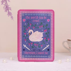 May include: A rectangular purple card featuring a white swan centered within a heart-shaped vine of pink flowers. The text reads, "the world can be cruel" and "therefore, i won't be," with two white daggers and a pink barbed wire border.