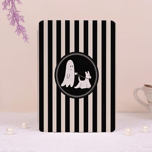 May include: A rectangular card featuring a vertical black and white striped pattern. In the center, a circular black emblem displays a white line-art illustration of a ghost walking a small dog on a leash, set against a solid black background.