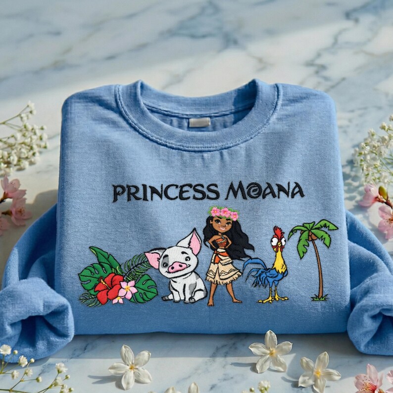 A blue t-shirt with a design featuring characters from the Disney movie " princess Moana" and tropical flowers.