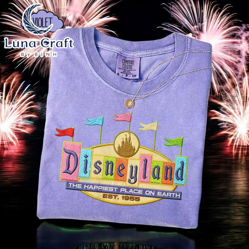 a purple t-shirt with a Disneyland logo and text, set against a background of fireworks.