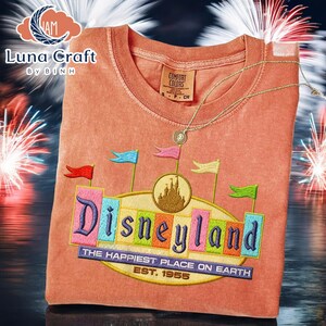 a t-shirt with a Disneyland logo, including a castle and fireworks, against a background of colorful fireworks.