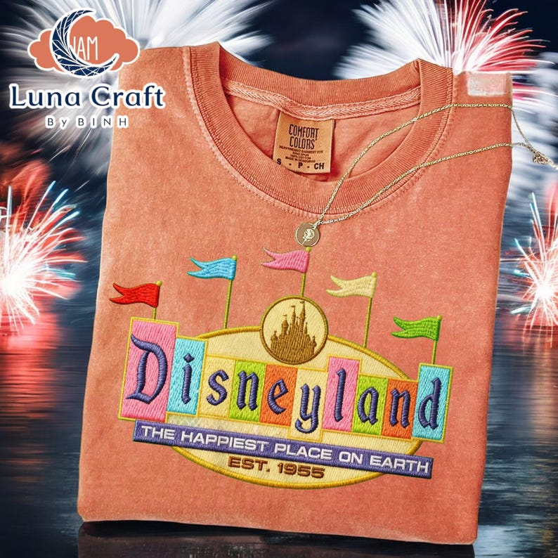 a t-shirt with a Disneyland logo, including a castle and fireworks, against a background of colorful fireworks.