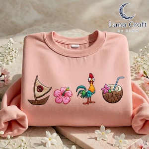 A pink sweater with various colorful and whimsical embroidered designs, including a sailboat, a flower, a coconut, and a rooster, all set against a floral background.
