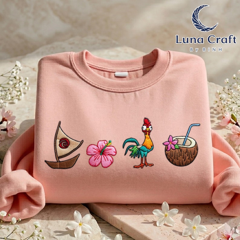 A pink sweater with various colorful and whimsical embroidered designs, including a sailboat, a flower, a coconut, and a rooster, all set against a floral background.