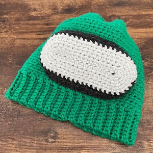Puede incluir: Gorro de punto de color verde con un diseño ovalado blanco y negro.