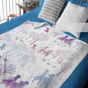May include: White blanket with a watercolor design featuring silhouettes of figures and trees in shades of purple, blue, and pink. The blanket is folded over a blue bed, with pillows visible.