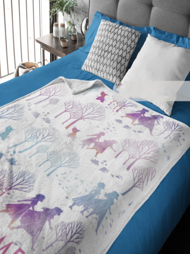 May include: White blanket with a watercolor design featuring silhouettes of figures and trees in shades of purple, blue, and pink. The blanket is folded over a blue bed, with pillows visible.