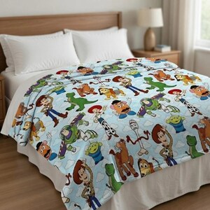 May include: A light blue blanket featuring various characters from the animated film "Toy Story." The blanket showcases characters like Woody, Buzz Lightyear, and Rex, set against a backdrop of white clouds. The blanket is spread over a bed.