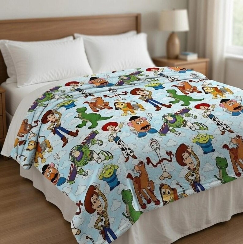 May include: A light blue blanket featuring various characters from the animated film "Toy Story." The blanket showcases characters like Woody, Buzz Lightyear, and Rex, set against a backdrop of white clouds. The blanket is spread over a bed.