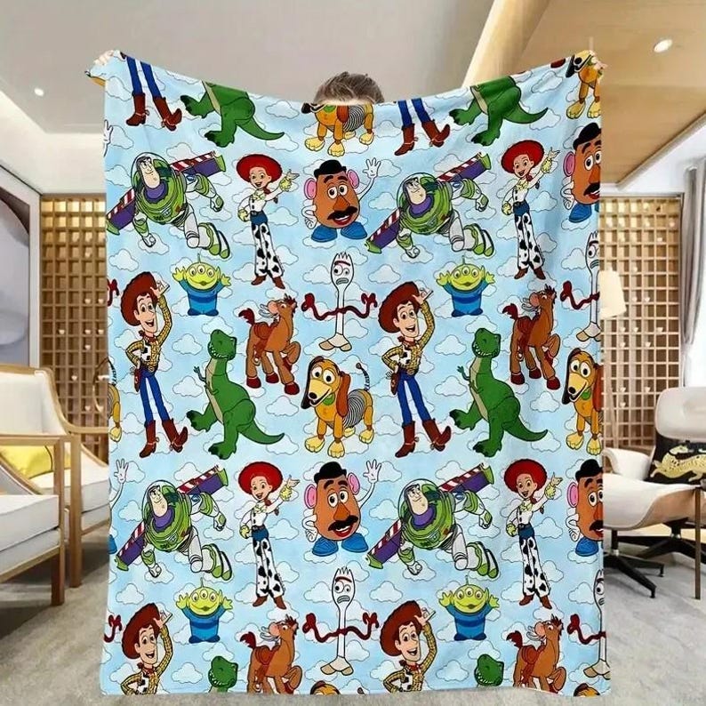 May include: A light blue blanket featuring a repeating pattern of characters from the animated film Toy Story. The design includes Woody, Buzz Lightyear, Jessie, Mr. Potato Head, Rex, Slinky Dog, and other characters. The blanket has a cloud-filled sky background.