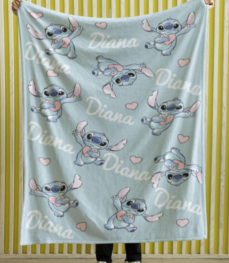May include: A light blue fleece blanket featuring a repeating pattern of the character Stitch holding a pink heart, interspersed with small pink hearts and the name Diana written in a white cursive script across the fabric surface.