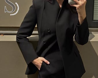 May include: A black blazer with a double-breasted design and a notched lapel. The blazer has two visible buttons and a pocket. The image also shows a matching black skirt or pants. The overall style is professional and tailored.