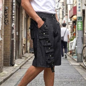 Puede incluir: Pantalones cortos cargo de mezclilla oscura con m&uacute;ltiples bolsillos y detalles de botones plateados. Los pantalones cortos tienen cremallera y trabilla para el cintur&oacute;n. Los pantalones cortos son hasta la rodilla y tienen un estilo casual.