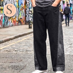 Peut inclure: Jean en denim noir et gris à jambes larges. Le jean présente un motif bicolore, avec une teinte plus foncée à l'avant et un gris plus clair sur les côtés. Il comporte des poches et une fermeture classique à bouton et fermeture éclair.