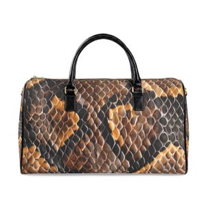May include: A travel duffel bag featuring a snakeskin print in brown, black, and tan. It has a black handle and trim, with a gold zip. The bag is rectangular and designed for carrying luggage or other items.