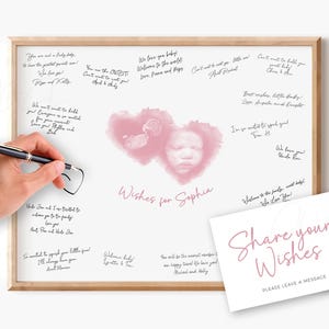 Puede incluir: Un libro de visitas para baby shower enmarcado con un marco de madera clara. La obra de arte presenta un diseño de corazón rosa con la imagen de un bebé y las palabras "Wishes for Sophia". Una mano sostiene un bolígrafo, lista para escribir un mensaje. Una tarjeta dice "Share your Wishes".
