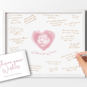 Puede incluir: Un letrero enmarcado en blanco con una imagen en forma de corazón rosa de la cara de un bebé, rodeado de deseos escritos a mano en tinta dorada. Una tarjeta más pequeña dice "Share your Wishes". Una mano escribe en el letrero.