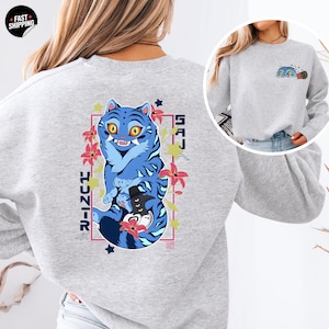 May include: A light gray sweatshirt featuring a blue tiger graphic with yellow eyes and black stripes. The design includes Japanese text and pink floral accents. A smaller version of the tiger design is on the upper right chest.