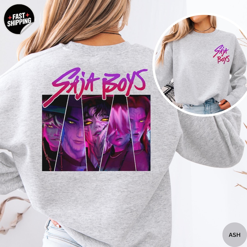 May include: Light gray sweatshirt with the text "Saja Boys" in a pink and purple font. The back of the sweatshirt features a graphic of four stylized faces. A smaller version of the text is on the upper right chest.