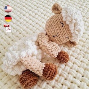 May include: A handmade, plush sheep toy in shades of white, tan, and brown. The sheep has a fluffy white head and body, with tan legs and a brown, textured hoof. The toy is lying on a white, woven blanket.