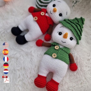 Può includere: Due pupazzi di neve all'uncinetto con corpo bianco, naso arancione e occhi neri. Uno indossa un gilet rosso e muffole rosse con piedi neri, l'altro un gilet verde, un cappello verde, braccia marroni, muffole rosse e piedi rossi con bottoni.