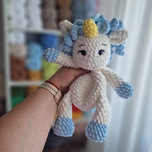 Può includere: Un giocattolo unicorno di peluche fatto a mano in bianco, blu e giallo. L'unicorno ha una criniera e una coda soffici, con accenti blu sugli zoccoli e sulle braccia. Ha un corno giallo e occhi neri.
