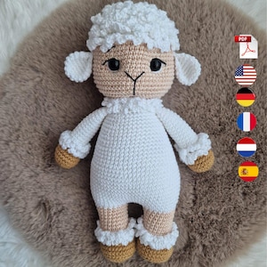 May include: A crocheted stuffed sheep toy with a white curly head and body, tan face, tan hands, and tan feet. The sheep has large black eyes and a stitched black nose and mouth. A PDF icon and several circular national flag icons are visible.