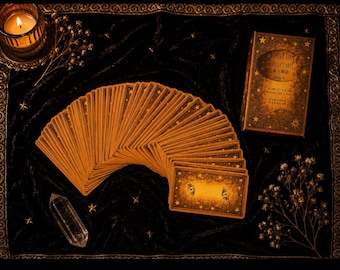 Puede incluir: Un mazo de cartas oráculo abanicado con dorsos dorados que presentan patrones de estrellas, junto a una caja rectangular etiquetada como Aurora Fate Oracle Cards, un cristal de cuarzo transparente y una vela encendida sobre tela de terciopelo.