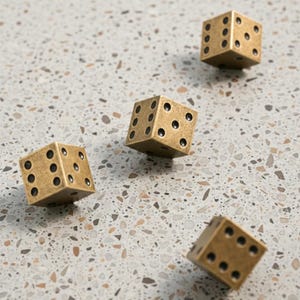 May include: Four brass dice with black dots are scattered on a speckled surface. The dice are cube-shaped, with each face displaying a different number of dots. The dice appear to be made of metal and have a slightly aged appearance.