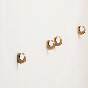 May include: A close-up of a white cabinet door with four brass-colored, ring-shaped drawer pulls. The pulls are evenly spaced and mounted vertically on the door. The cabinet door has vertical lines.