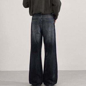 May include: Dark wash denim jeans with a wide leg design. The jeans have a faded effect, transitioning from a lighter shade at the waist to a darker shade towards the hem. The back pockets are visible.