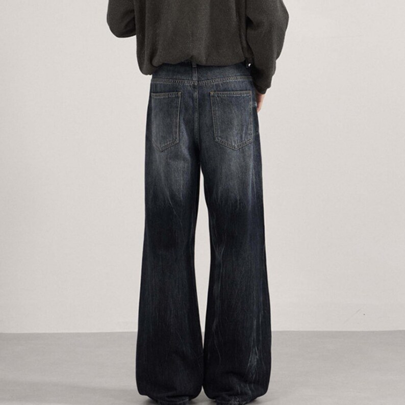 May include: Dark wash denim jeans with a wide leg design. The jeans have a faded effect, transitioning from a lighter shade at the waist to a darker shade towards the hem. The back pockets are visible.