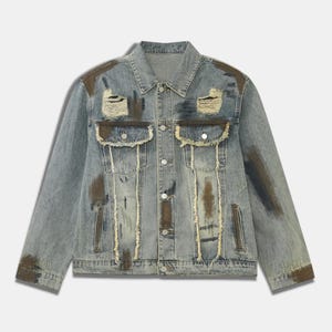 May include: Light blue denim jacket with distressed detailing. Features ripped sections, brown paint-like accents, and button closures. Includes two chest pockets and two side pockets. A casual, vintage-inspired outerwear piece.