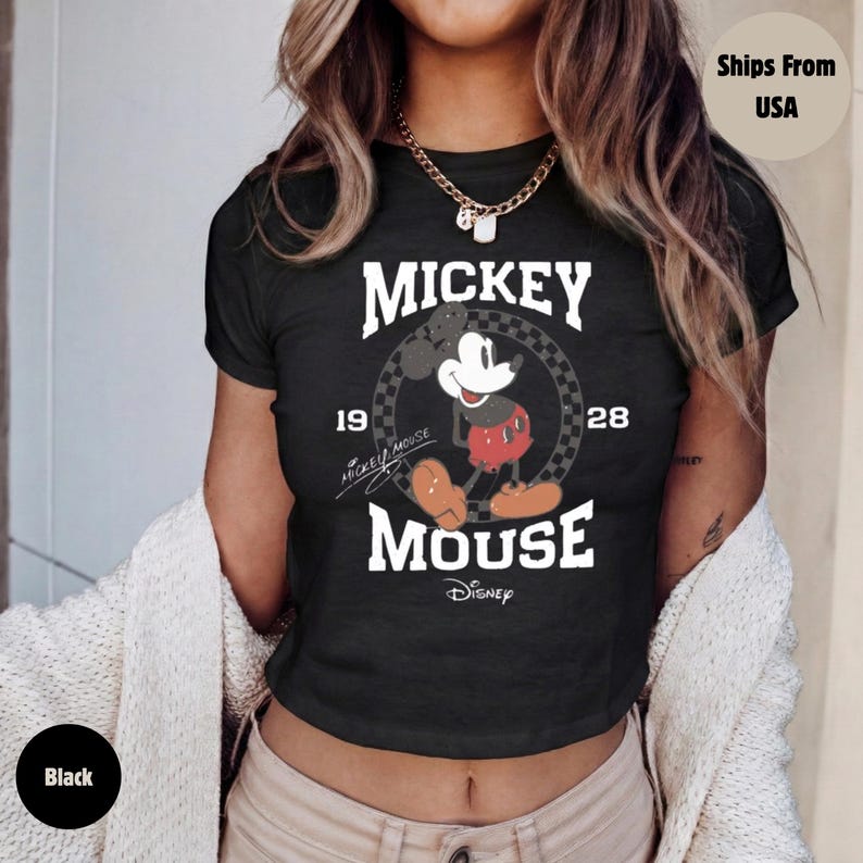 May include: Black crop top featuring a Mickey Mouse graphic. The design includes the words "Mickey Mouse" in white, along with the year "1928" and an image of Mickey Mouse. The shirt is a classic Disney design.