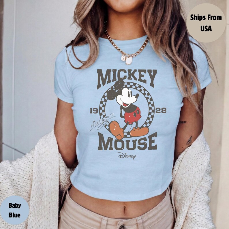 May include: Baby blue crop top featuring a distressed graphic of Mickey Mouse. The design includes the words "Mickey Mouse" and "Disney" with the years 1928 and 1919. The shirt has short sleeves and a crew neck.