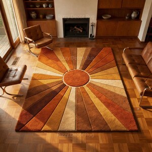 May include: A large, rectangular rug with a sunburst design in shades of brown, orange, and beige. The rug features a central circular element and radiating stripes, creating a warm aesthetic. The rug is placed on a wooden floor.