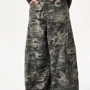 Peut inclure: Pantalon cargo camouflage dans les tons de vert, gris et noir. Le pantalon à jambes larges comporte deux grandes poches cargo et une ceinture noire. Le pantalon est fait d'un tissu durable.