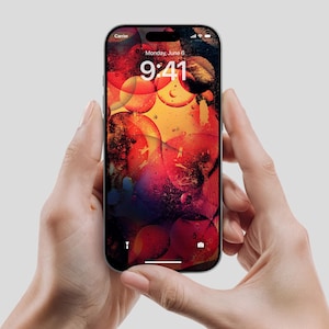 Könnte beinhalten: Ein Smartphone, gehalten in zwei Händen, zeigt einen farbenfrohen abstrakten Hintergrund mit roten, orangen und violetten Farbtönen. Der Bildschirm zeigt die Uhrzeit 9:41 Uhr am Montag, den 6. Juni.