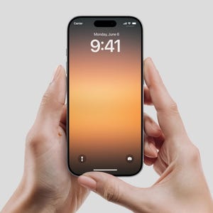 Könnte beinhalten: Ein schwarzes Smartphone mit einem Bildschirm, der die Uhrzeit, das Datum und einen Hintergrund mit Farbverlauf in Orange- und Gelbtönen anzeigt. Das Telefon wird von zwei Händen vor einem hellgrauen Hintergrund gehalten.
