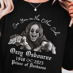 May include: Black sweatshirt featuring a graphic of Ozzy Osbourne with the text "See You on the Other Side." The design includes the text "Ozzy Osbourne 1948 ∞ 2025 Prince of Darkness."
