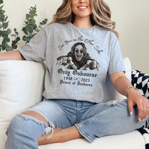 Może przedstawiać: Szara koszulka z czarno-białym zdjęciem Ozzy'ego Osbourne'a i napisem "See You on the Other Side". Poniżej obrazu widnieje napis "Ozzy Osbourne 1948 &infin; 2025 Prince of Darkness".