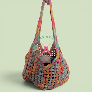 May include: A colourful, handmade crochet tote bag with a large open weave. The bag is made with a mix of pink, orange, yellow, and green yarn. It has long straps and is filled with a fluffy white item and other items.