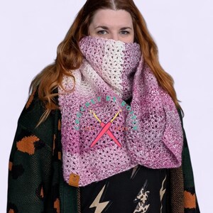 Könnte beinhalten: Handgefertigter Häkelschal in Rosa- und Weißtönen. Der Schal ist um den Hals gewickelt. Das offene Webmuster ist sichtbar. Ein kleines Lederetikett ist angebracht. Der Text "MADE BY ROO" ist auf dem Schal zu sehen.