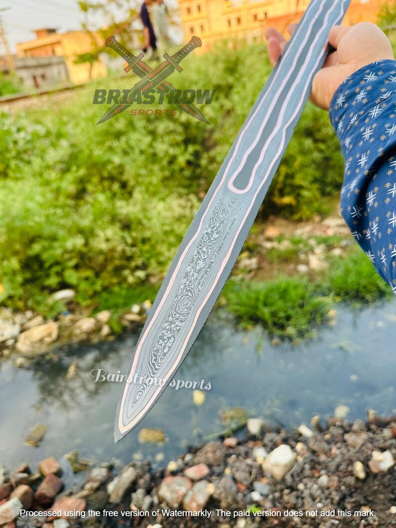 May include: A double-edged sword blade featuring a central panel with a complex, swirling Damascus steel pattern, bordered by smooth, light-colored metal edges. The blade displays the text Briastrow Sports and Bairstrow sports.