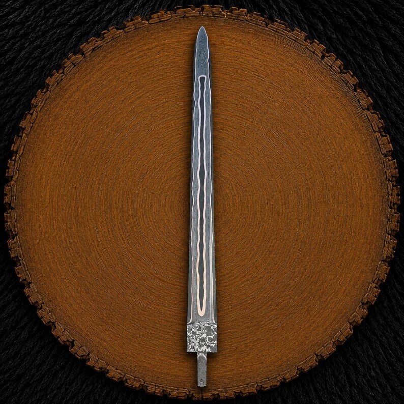 May include: A double-edged dagger blade featuring a dark, layered Damascus steel pattern with a central copper inlay running vertically along the length. The blade has a pointed tip and a textured, rectangular tang at the base for handle attachment.