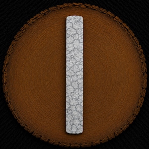 May include: A rectangular metal bar with rounded ends, featuring a textured, silver-toned surface with a repeating, intricate floral-like pattern. The object is positioned vertically, displaying a consistent metallic finish across its entire length.
